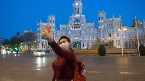 Una joven con mascarilla se hace un selfi delante de la Cibeles en un Madrid prácticamente vacío en las primera horas del Estado de Alarma decretado por el Gobierno por el coronavirus. E.P./Joaquin Corchero