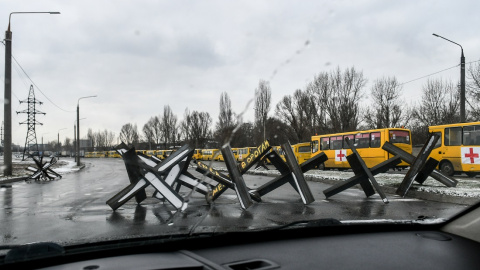 Obstáculos antitanque, conocidos como erizos checos, bloquean una calle cerca de un convoy de autobuses listos para despegar hacia la sitiada Mariupol para entregar ayuda humanitaria y evacuar a la gente.