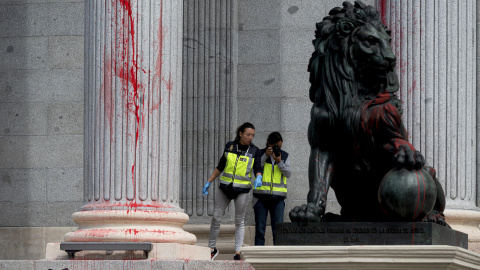 Efectivos de la Policía Nacional inspeccionan uno de los leones del Congreso, cubierto con pintura roja tras la acción reivindicativa de un grupo de activistas