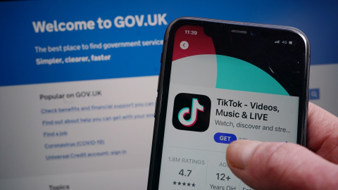 Un usuario se descarga TikTok en su teléfono móvil mientras consulta la página web del Gobierno de Reino Unido.