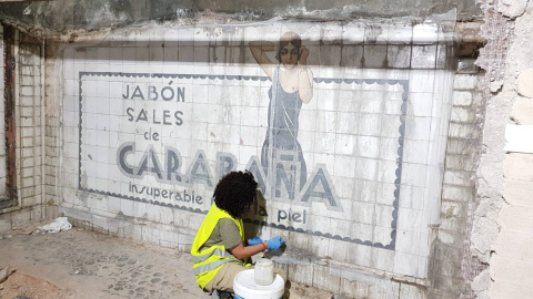 Operaria limpia los azulejos del mural publicitario datado en los años 20 y descubierto en las obras de la estación de metro Sevilla, en Madrid. / Consejería de Cultura