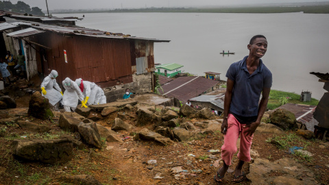 Eric Gweah, 25, observa como los miembros del equipo de entierros de la Cruz Roja llevan el cuerpo de su padre, Ofori Gweah, 62, una victima del Ébola, en la zona del rio Rock Spring Valley en Monrovia central, Liberia./ REUTERS/Daniel Bere