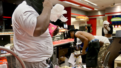 Un saqueador armado con una pistola en la cintura roba artículos de un QuikTrip después de los disturbios que estallaron al final de una vigilia por Michael Brown en Ferguson , Missouri en agosto de 2014.  El St. Louis Post-Dispatch ha reci