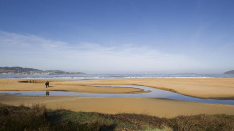 Dos personas pasean por la playa América en el ayuntamiento de Nigrán, Pontevedra.