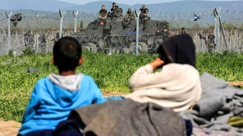 Varios niños descansan en Idomeni junto a la frontera, mientras la Policía macedonia hace guardia al otro lado de la valla. - EFE