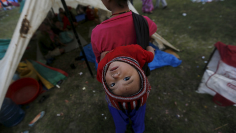 Una víctima del terremoto lleva a su bebe en la espalda mientras permanece fuera de su refugio improvisado en las afueras de Katmandú./  REUTERS/Adnan Abidi