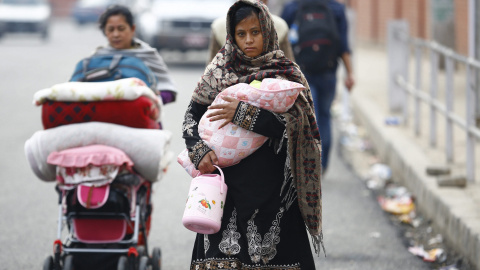 Una mujer lleva a su hijo en brazos mientras su madre carga con un carrito lleno de mantas al regresar a su casa en Katmandú./ EFE/Narendra Shrestha