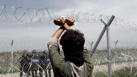 Un refugiado permanece tras la valla fronteriza frente a un grupo de policías macedonios durante una protesta en el campo de refugiados de Idomeni, situado en la frontera entre Macedonia y Grecia. EFE/Kostas Tsironis