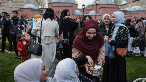 Una mujer ofrece dulces a otras mujeres musulmanas reunidas frente a la Mezquita Azul tras participar en las oraciones del Eid al-Fitr, en Estambul, a 21 de abril de 2023.