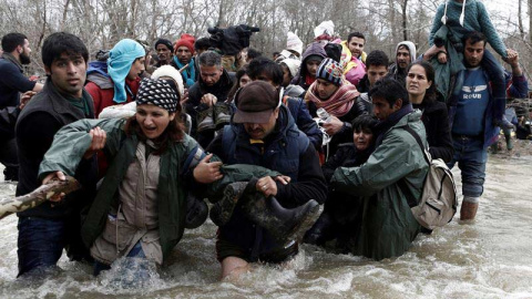 Varios refugiados  usan una cuerda para cruzar un río en la frontera entre Grecia y Macedonia. / YANNIS KOLESIDIS (EFE)