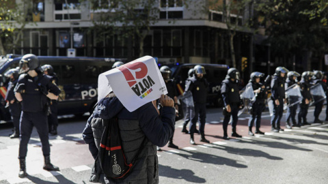 Una persona con un cartel en favor del Sí en el referéndum del 1-0 pasa delante de los antidisturbios de la Policái Nacional desplegadas ante la se sede del CUP. | XAVI HERRERO