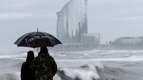 Dos personas observan el oleaje en la playa de la Barceloneta, hoy domingo, donde el Ayuntamiento de Barcelona ha activado este fin de semana, en fase de alerta el Plan básico de Emergencia Municipal