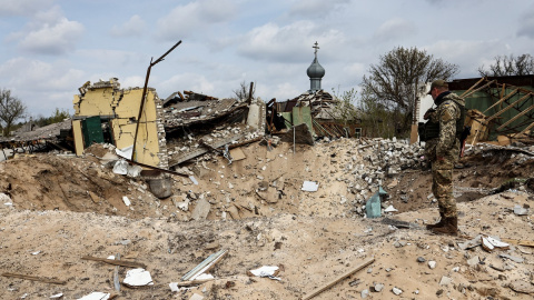 16/04/2022 Un militar ucraniano mira jacia un cráter y una casa destruida en la localidad de Yatskivka, en el este del país