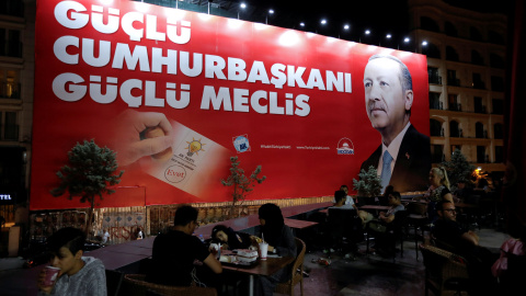 Personas en la terraza de un restaurante mientras, de fondo se puede ver un cartel preelectoral de Erdogan. - REUTERS