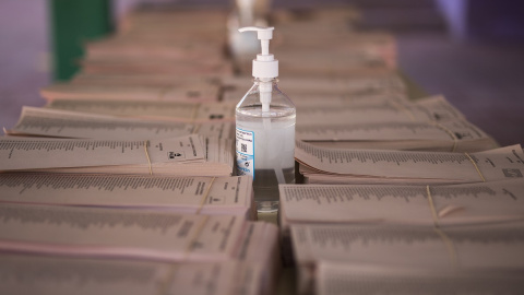 Un bote de gel hidroalcohólico corona una mesa llena de papeletas electorales en el Colegio Público Asturias en el distrito Puente de Vallecas, a 4 de mayo de 2021, en Madrid