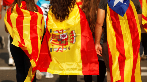 Tres jóvenes caminan por barcelona con la senyera, la bandera de España y la estelada.- REUTERS