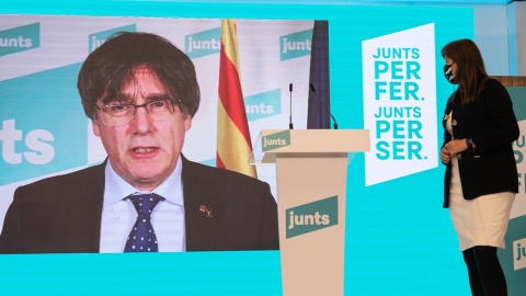 La número 2 de JxCat por Barcelona, Laura Borrás, observa al número 1 del partido por Barcelona, Carles Puigdemont (pantalla), durante una rueda de prensa para valorar los resultados obtenidos por su formación en los comicios catalanes dura