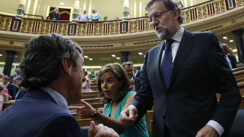 El presidente del Gobierno, Mariano Rajoy, conversa con el portavoz parlamentario del PP, Rafael Hernando, en presencia de la vicepresidenta, Soraya Sáenz de Santamaría, tras finalizar la votación en la que se rechazaron todas las enmiendas