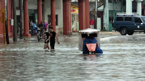 Varias personas caminan por una calle llena de agua, hoy en La Habana