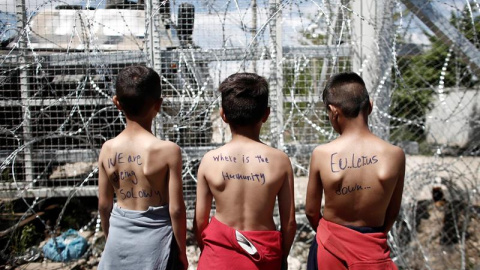 Un grupo de niños con mensajes en sus espaldas en los que se leen "Estamos muriendo lentamente", "¿Dónde está la humanidad?" y "La UE nos falla" participa en una protesta en el campamento de refugiados de Idomeni, Grecia. EFE/Kostas Tsironi