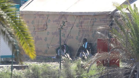 Dos hombres se protegen del sol en la sombra de una tienda del centro para migrantes de Barranco Seco, en Gran Canaria.