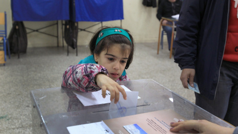 Una niña introduce en la urna el voto de sus padres en un colegio electoral en Atenas. EFE/EPA/SIMELA PANTZARTZI