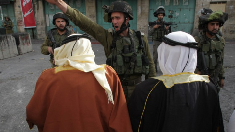 Un soldado israelí da órdenes a dos hombres palestinos durante una manifestación en Hebrón. - AFP