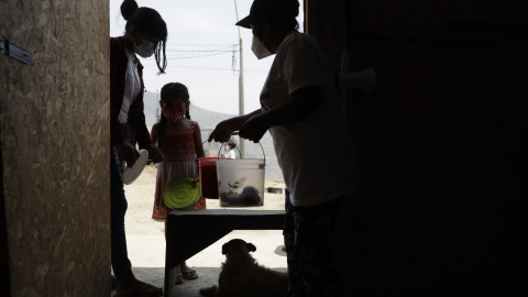 Una mujer y una niña reciben alimentos en el asentamiento humano de Buena Vista el 2 de febrero de 2021, en el populoso distrito limeño de Villa María del Triunfo, en Lima (Perú).