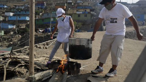 Dos personas cargan una olla en el asentamiento humano de Buena Vista el 2 de febrero de 2021, en el populoso distrito limeño de Villa María del Triunfo, en Lima