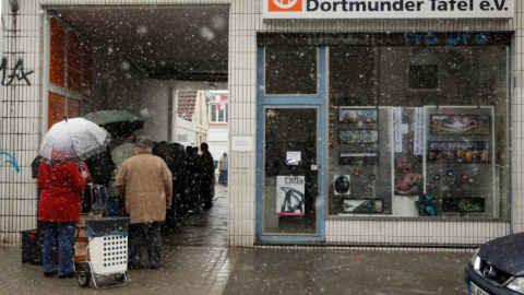 Varias personas guardan cola para recoger alimentos mientras nieva en la ciudad de Dortmund./REUTERS