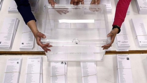 Tres personas sujetan una urna sobre las papeletas en un colegio electoral. EFE