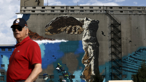 Un hombre pasa por delante de una pintada que reproduce la estatuta de la Vcotira de Samotracia, cerca del puerto del Pireo, en Atenas. REUTERS/Alkis Konstantinidis