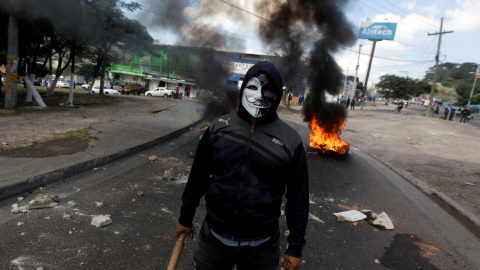 Un manifestante enmascarado mira a la cámara mientras unos neumáticos arden al fondo. REUTERS/Jorge Cabrera