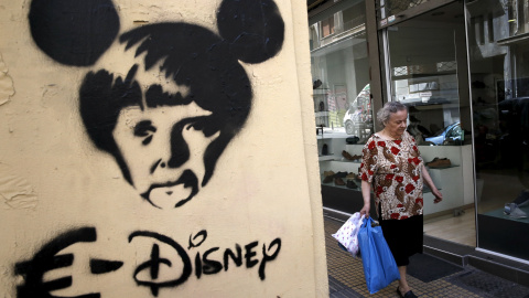 Una mujer con las bolsas de la compra pasa, en Atenas, junto a una pintada con una carictura de la canciller alemana Angela Merkel. REUTERS/Alkis Konstantinidis