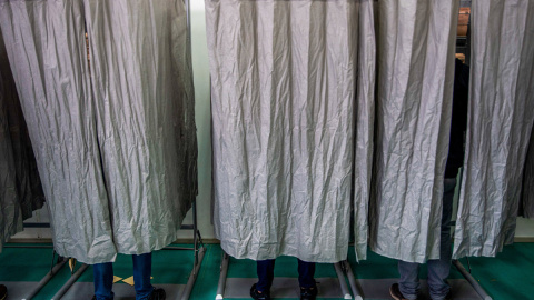 Tres personas ejercen su voto en secreto dentro de las cabinas dispuestas en un colegio electoral.