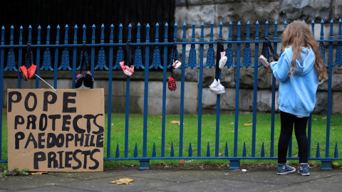 Una niña de espaldas junto a pancarta en la que dice que ""El Papa protege a los curas pederastas" en Dublín. /REUTERS