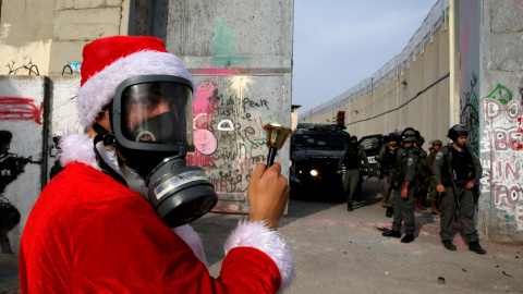 Un manifestante palestino vestido de Papá Noel protesta ante tropas israelíes en el muro que rodea la ciudad de Belén, ayer sábado 23 de diciembre. REUTERS/Ammar Awad