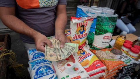 Un hombre muestra billetes de dolar en un puesto de venta de comida el 5 de febrero de 2021, en Caracas (Venezuela).