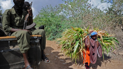 Una mujer somalí acarrea productos agrócolas junto a varios soldados que patrullan cerca de Mogadiscio. AFP / MOHAMED ABDIWAHAB