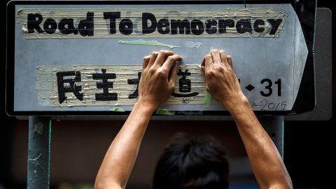 Un trabajador retira la cinta adhesiva de una señal en la que los manifestantes han escrito 'Camino a la democracia', durante el último 'Occupy' en Hong Kong. /ATHIT PERAWONGMETHA (REUTERS)