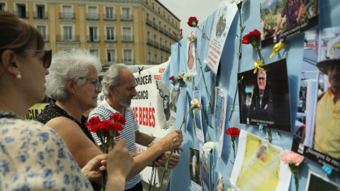 (22/5/22) Varias personas colocan claveles en un mural con retratos de colaboradores en la búsqueda de víctimas por el robo de bebés en España, a 22 de mayo de 2022.