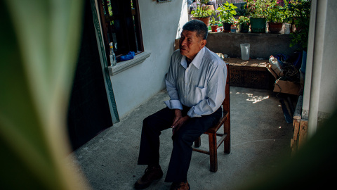 Román Coc sentado en una silla de madera en el patio que separa la cocina comedor de las habitaciones.