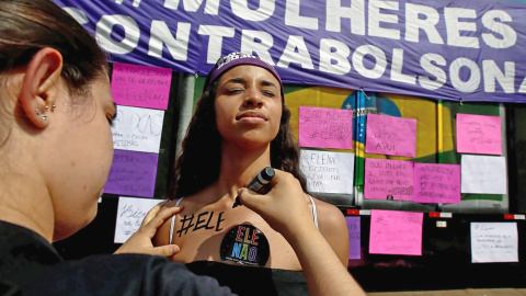 Una mujer pinta en la piel de otra: 'Él no', durante las manifestaciones contra Bolsonaro este sábado en Sao Paulo. REUTERS