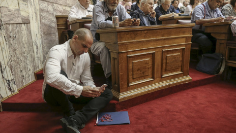 El ministro griego de Finanzas, Yanis Varoufakis consulta su móvil sentado en el suelo durante la intervención del primer ministro, Alexis Tsipras, ante el grupo parlamentario de Syriza. REUTERS/Costas Baltas