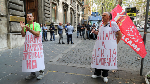 Dos personas protestan frente al Ministerio de Trabajo italianl, en Roma, con sendas pancartas que dicen "Queremos dignidad para los trabajadores" y "Tenemos trabajo, pero no sueldo". REUTERS/Tony Gentile