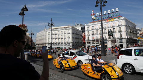 Un hombre fotografía con su móvil a un vehículos para turistas que pasan por la madrleña Puerta del Sol. REUTERS/Susana Vera