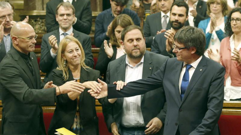 El presidente de la Generalitat, Carles Puigdemont, saluda a los consellers Neus Munté y Raül Romeva en el pleno del Parlament. - EFE