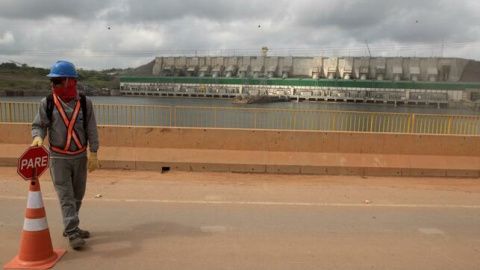 Un hombre sostiene un cartel en el puente que cruza el río Xingu, con la hidroeléctrica de Belo Monte al fondo (Brasil) | EFE