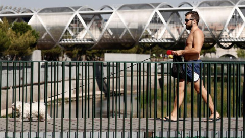 Un hombre pasea a su perro por una de las pasarelas de Madrid Río, que cruza el Manzanares paralela al icónico puente de Arganzuela, diseñado por el arquitecto francés Dominique Perrault, esta calurosa mañana de sábado de agosto. EFE/MARISC