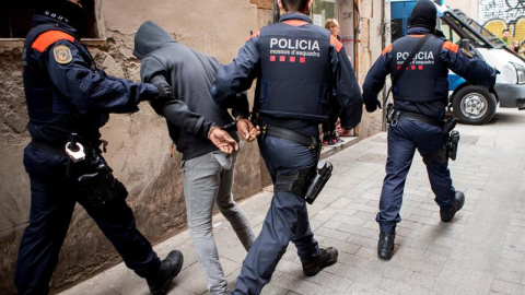 Los Mossos d'Esquadra custodian a uno de los detenidos en la operación contra el narcotráfico en Barcelona que incluye unos cuarenta registros de "narcopisos". /EFE